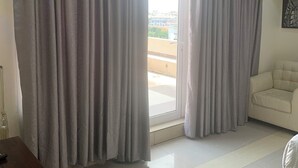 A room with a large window, a sofa, a wooden table, and a chair. - City Residence Lagos (Lagos)