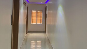 A hallway with a wooden door on the left, a window with blinds in the center, and recessed lighting with blue LED strips on the ceiling. - City Residence Lagos (Lagos)