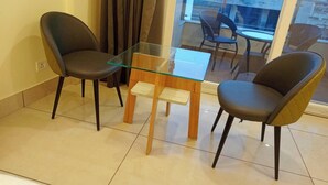 Un balcón con una mesa de vidrio y dos sillas, vistas de la ciudad y una ventana con cortinas.