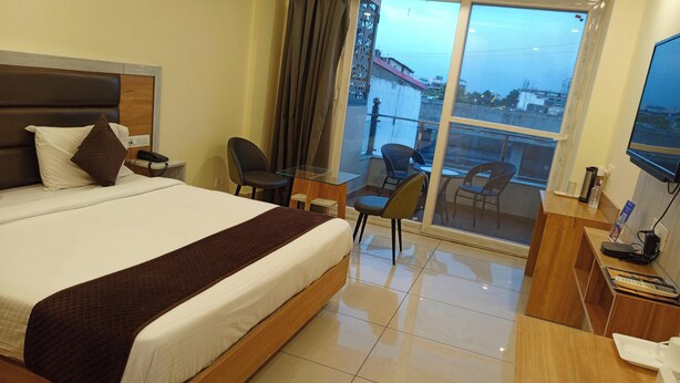 Habitación de hotel con una cama grande, un escritorio, una silla, un televisor y un balcón con vista a la ciudad.