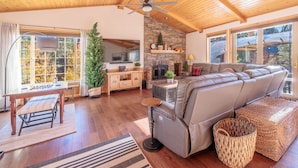 A spacious living room with a stone fireplace, a leather sofa, and a ceiling fan. - New! Bearadise ~ The Retreat (Big Bear Lake)