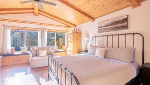A spacious bedroom with a large bed, a wooden ceiling, a window seat with a sofa, and a painting on the wall. - New! Bearadise ~ The Retreat (Big Bear Lake)