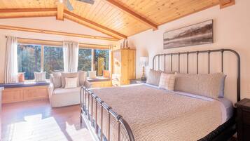 Un'ampia camera da letto con un letto grande, un soffitto in legno, una seduta finestrata con divano e un quadro appeso al muro.