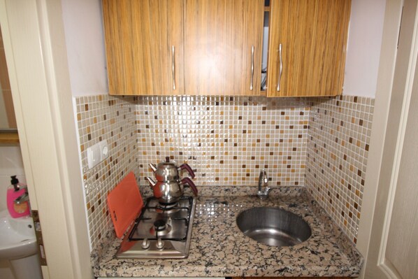 A kitchen with wooden cabinets, a tiled backsplash, a stainless steel sink, and a gas stove. - Avşa Anı Motel & Apart (Marmara)