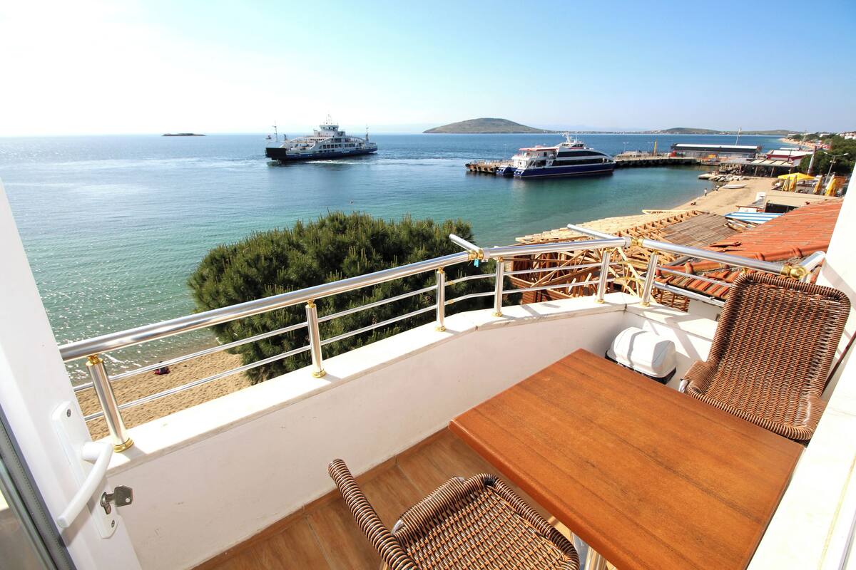 Ein Balkon mit Korbmöbeln, einem Holztisch und Blick auf das Meer mit Booten.