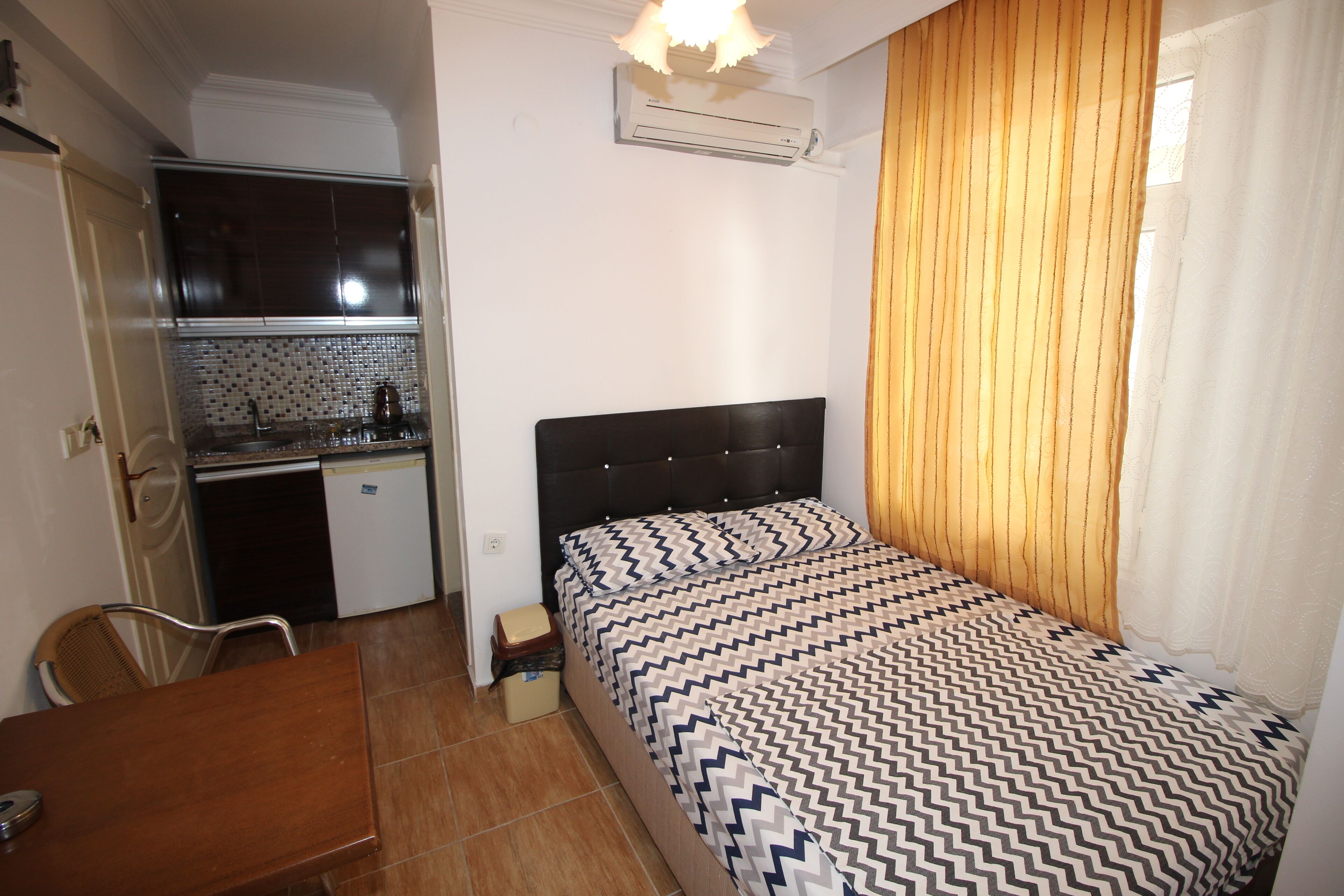 Une chambre d’hôtel de taille réduite, comprenant un lit, une petite kitchenette, une table à manger et une chaise.