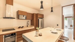 A modern kitchen with wooden cabinets, a central island, and a dining area with a table set for two. - 2br Jungle Retreat with Private Pool (Tulumn)