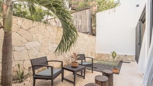An outdoor patio with stone walls, a palm tree, and a seating area with chairs and tables. - 2br Jungle Retreat with Private Pool (Tulumn)