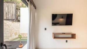 A modern room with a stone wall, a small potted plant, a wooden shelf, and a mounted TV. - 2br Jungle Retreat with Private Pool (Tulumn)