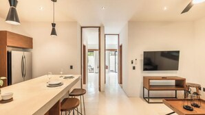 A modern kitchen with a central island, bar stools, a dining table set for two, and a flat-screen TV mounted on the wall. - 2br Jungle Retreat with Private Pool (Tulumn)