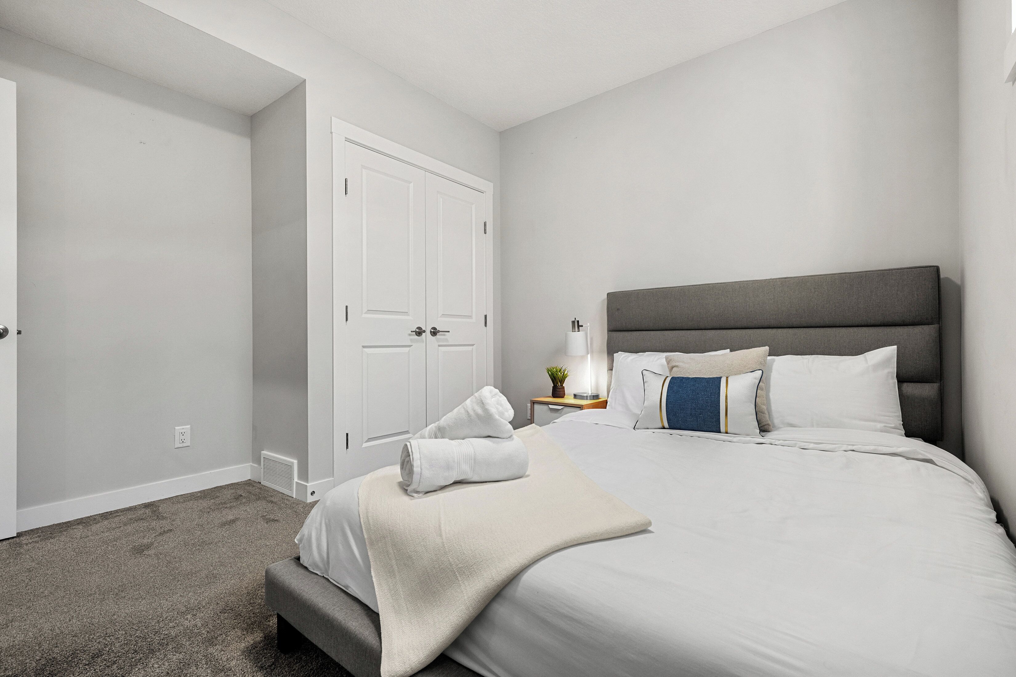 A bedroom with a bed, a bedside table with a lamp, and a wardrobe.