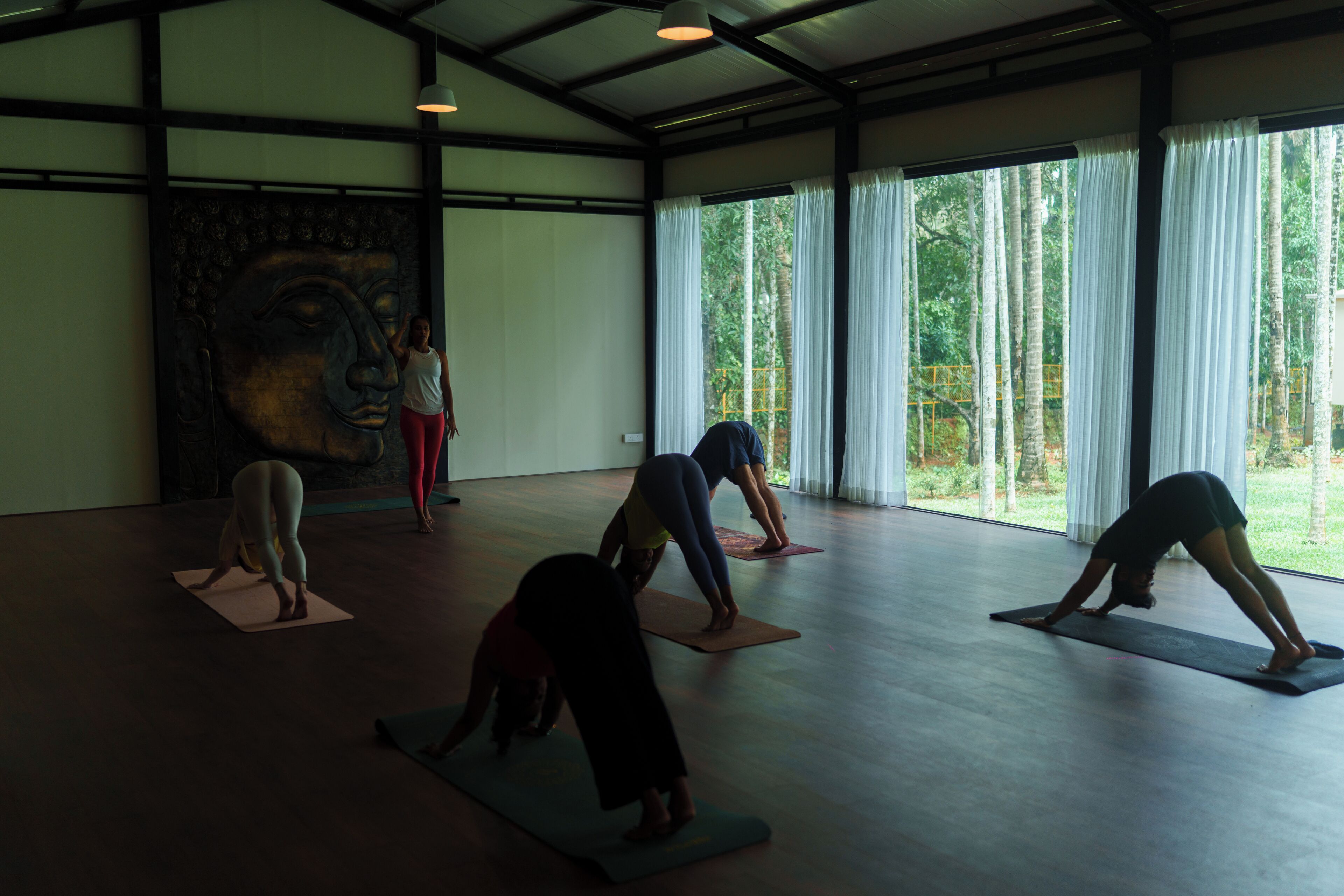 Une pièce spacieuse avec de grandes fenêtres, une fresque murale et des personnes pratiquant le yoga.