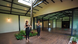 A spacious indoor area with a high ceiling, wooden flooring, and potted plants. - Hipnoetic Goa -Private Pool Cottages (Quepem)