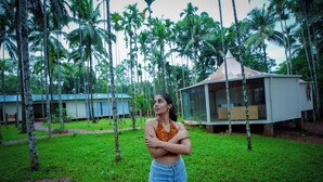A person standing in a grassy area with palm trees and a building in the background. - Hipnoetic Goa -Private Pool Cottages (Quepem)