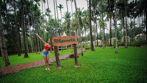 A sign with the word "Hipnoetic" in a tropical setting with palm trees and a grassy area. - Hipnoetic Goa -Private Pool Cottages (Quepem)