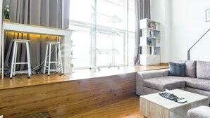 A modern living room with a wooden floor, a grey sofa, a white coffee table, and a white shelving unit. - Empire City Damansara M Tower by Airhost (Petaling Jaya)
