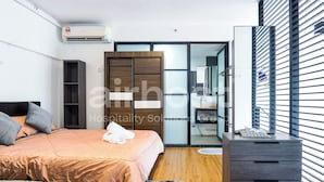 A modern hotel room with a bed, a wardrobe, a desk, and a bathroom visible through a glass door. - Empire City Damansara M Tower by Airhost (Petaling Jaya)