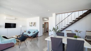 Een moderne woonkamer met een bank, een eettafel met stoelen, een trap en een flatscreen televisie aan de muur.