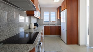 Een moderne keuken met granieten aanrechtbladen, houten kasten, een inbouwoven en een raam dat voor natuurlijk licht zorgt.
