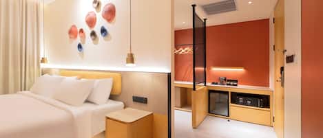 A modern hotel room with a large bed, a small desk, and a kitchenette.