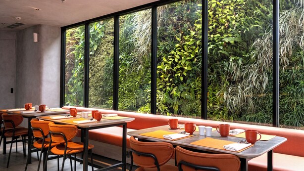 Un restaurante con amplios ventanales, asientos naranjas y mesas con manteles individuales anaranjados.