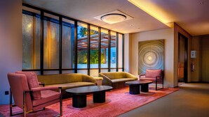 Un espacio lounge moderno con sofás, sillones y mesitas de centro, que cuenta con grandes ventanales y una llamativa obra de arte en la pared.