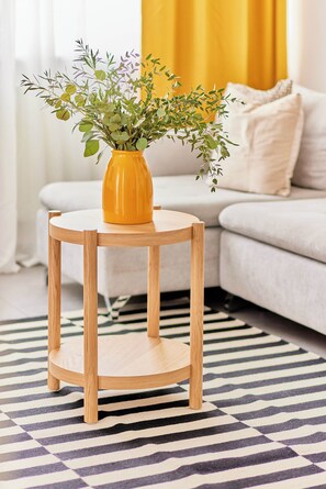 Una mesa redonda de madera con un florero de follaje verde.