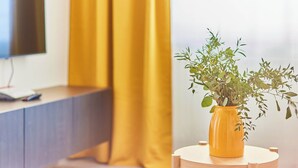 Een kamer met een geel gordijn, een houten bureau en een gele vaas met een plant.