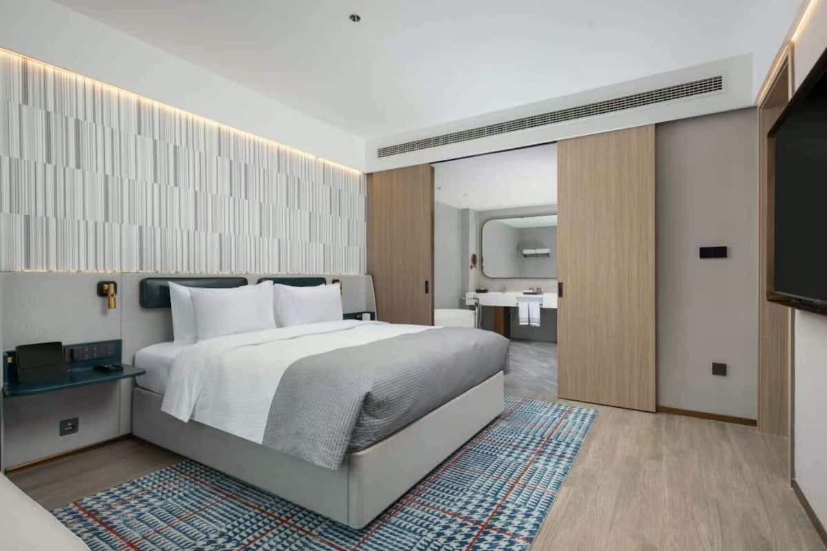 Un dormitorio moderno con una cama grande, mesitas de noche, un televisor integrado y un baño visible a través de una puerta abierta.