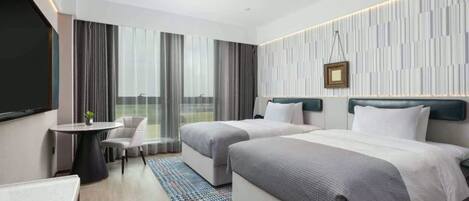 A hotel room with two beds, a desk, a chair, and a large window with curtains.
