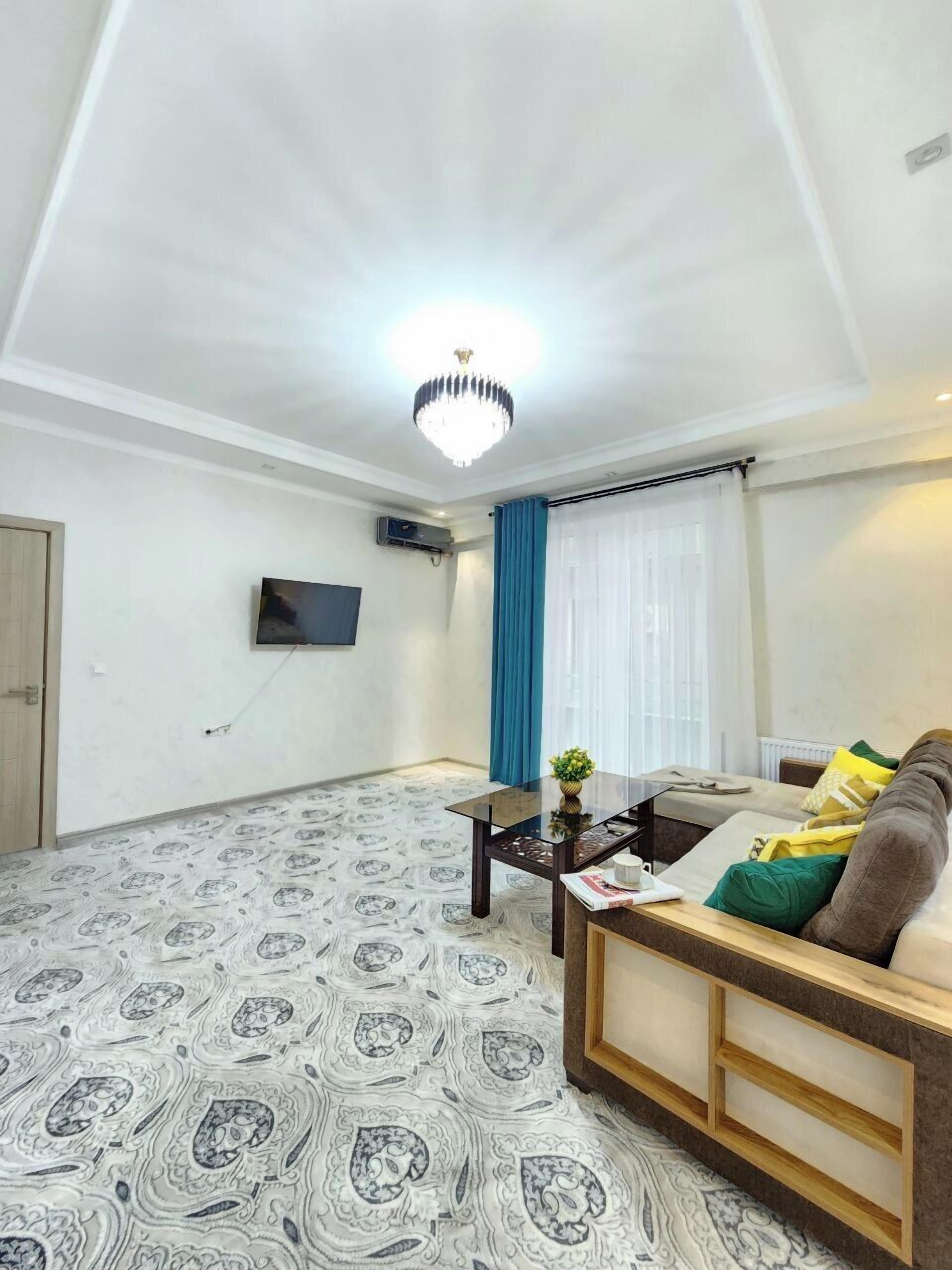 A living room with a patterned floor, a sofa, a coffee table, a TV mounted on the wall, and a ceiling light fixture.
