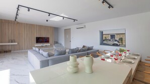 Ett modernt vardagsrum med en grå soffa, ett matbord dukat med rödvinsglas och en tv som är monterad på väggen.