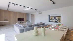 Ein modernes Wohnzimmer mit einem grauen Sofa, einem Esstisch mit Weingläsern und einem an der Wand befestigten Fernseher.
