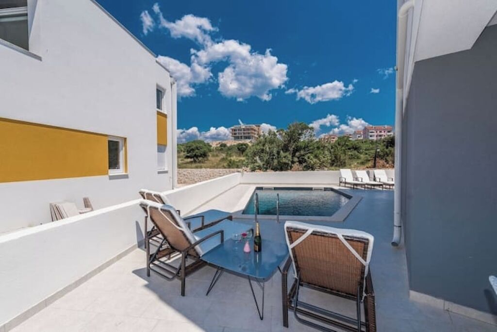 A rooftop pool area with a table and chairs, a view of the surrounding buildings, and a clear sky.