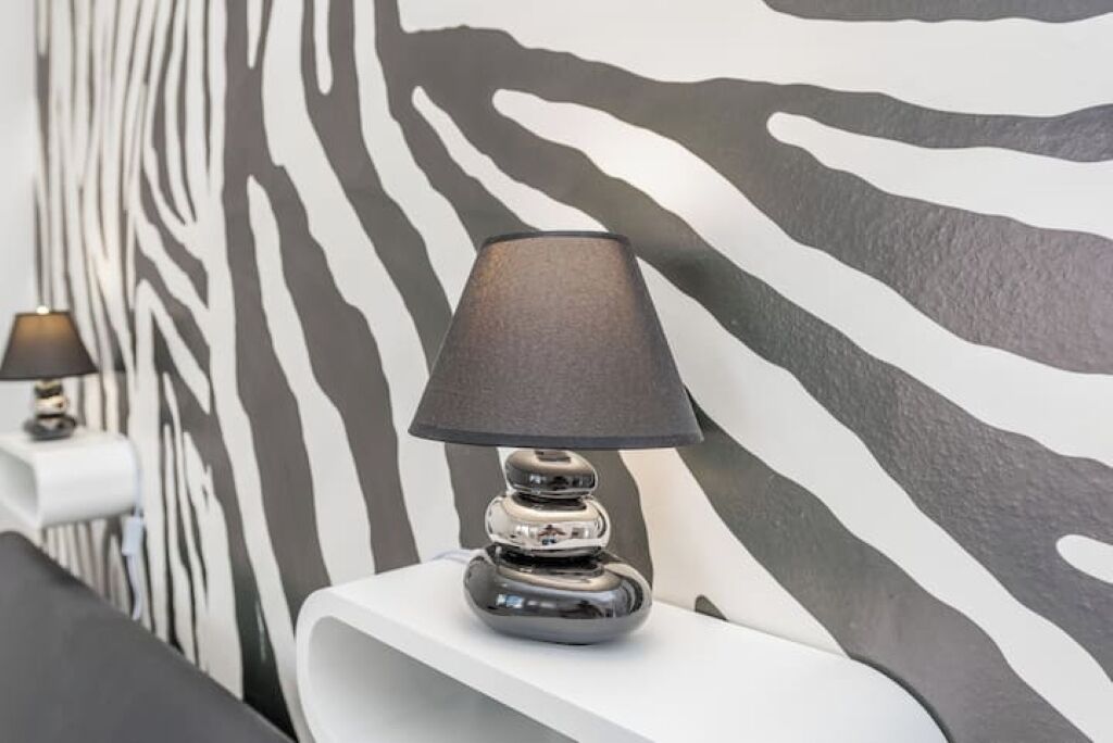 Una lámpara moderna sobre una mesita auxiliar blanca, con una pared estampada de cebra al fondo.
