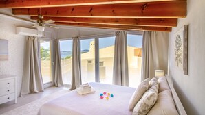 Una camera da letto con un letto grande, un ventilatore a soffitto e vista sul mare dalle finestre.