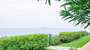 Un giardino curato con un vialetto in pietra che conduce a un cancello, con vista su uno specchio d'acqua e una montagna in lontananza.