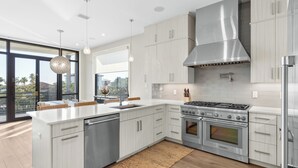 Cozinha moderna com uma ilha grande, eletrodomésticos de aço inoxidável e vista para o exterior.