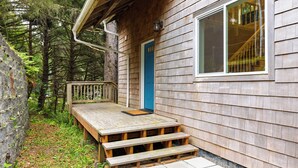 Eine Holzhütte mit blauer Tür, einer Holzdiele und einer Treppe zu einem Fenster.
