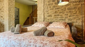 Un dormitorio con colcha estampada, cabecera de madera y pared de piedra.
