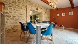 Un comedor con pared de piedra, una mesa blanca, sillas azules y una lámpara moderna.