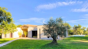 Et moderne hus med en stor forhave, et træ og en klar blå himmel.