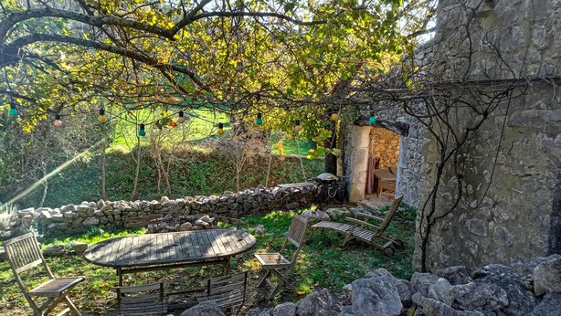 Un'area salotto esterna rustica con pareti in pietra, un tavolo di legno e sedie.