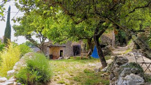 Un edificio rustico in pietra con una porta di legno, immerso nel verde e circondato da un muro in pietra.