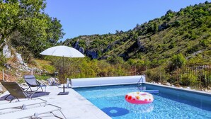 Una piscina con lettini e un ombrellone, immersa in un paesaggio montuoso.