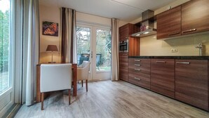 A modern kitchen with wooden cabinets, a dining area with a table and chairs, and a view through a glass door to the outdoors. - Cozy home in Lemele with heated swimming pool (Lemele)