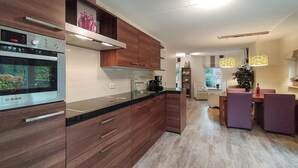 A modern kitchen with a Bosch oven, wooden cabinets, and a dining area with purple chairs. - Cozy home in Lemele with heated swimming pool (Lemele)