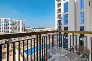 A balcony with a view of a swimming pool and construction site, overlooking a cityscape with high-rise buildings. - Chic 1BR | Next to Metro | Brand New | BMS (Dubai)