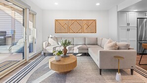 A modern living room with a sectional sofa, a round wooden coffee table, and a decorative wall panel. - Park City Getaway with Mountain Views, Hot Tub & Fire pit | High West Hideaway (Park City)