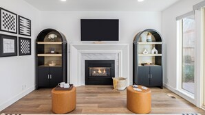 A modern living room with a fireplace, two wooden ottomans, and black shelving units with decorative items. - Park City Getaway with Mountain Views, Hot Tub & Fire pit | High West Hideaway (Park City)